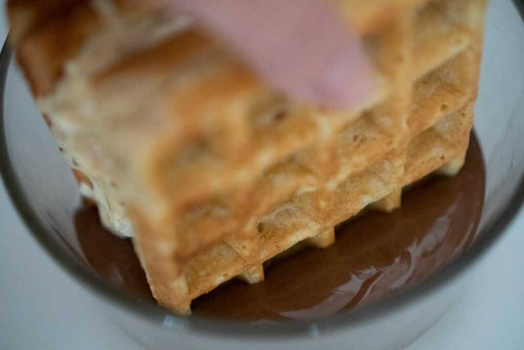 dipping waffle ice cream sandwich in melted chocolate