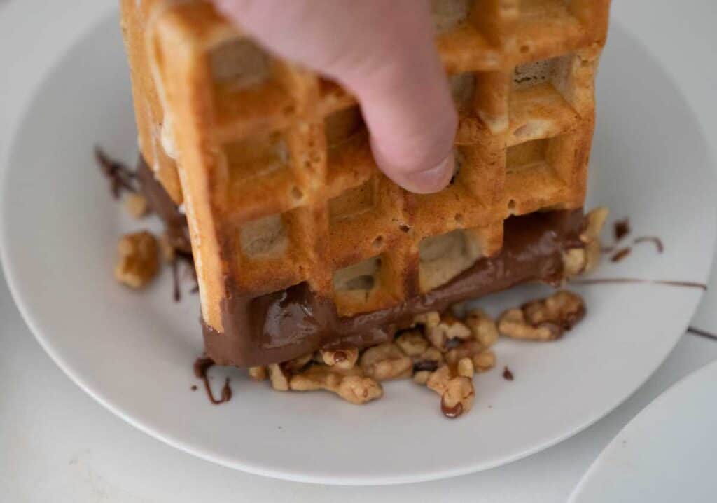 dipping waffle ice cream sandwich in walnuts