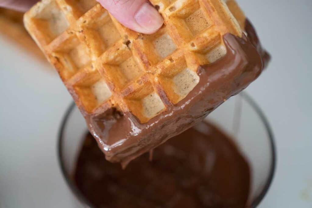 dipping waffle ice cream sandwich in melted chocolate