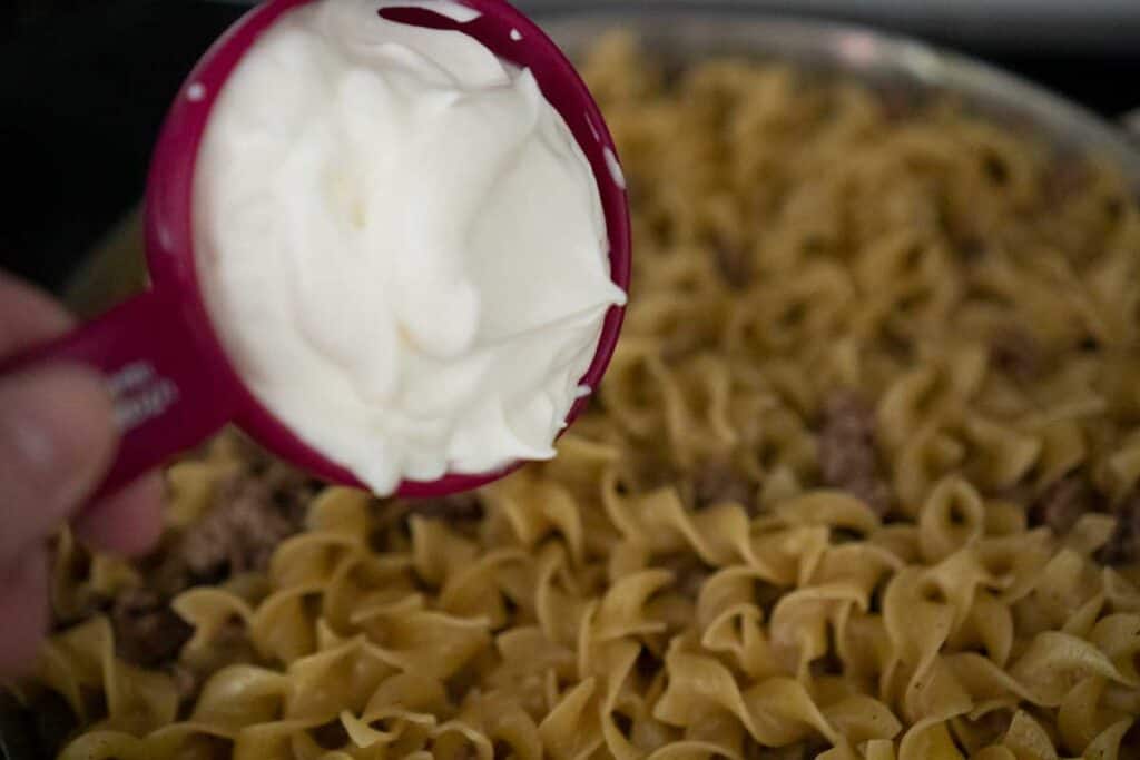 adding sour cream to pan of noodles