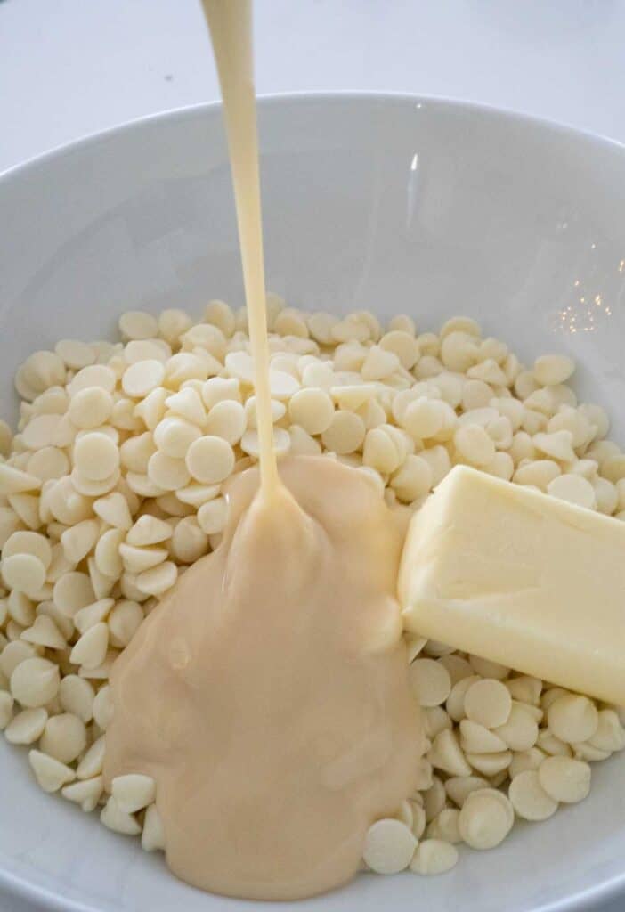 pouring condensed milk over white chocolate chips and butter