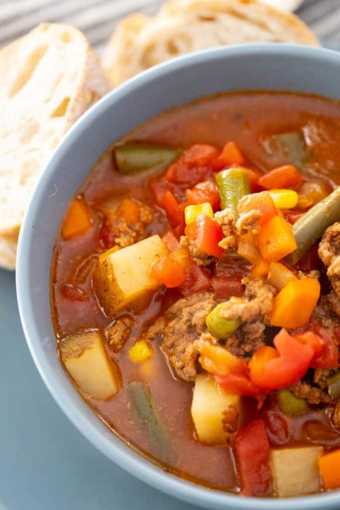 close up of blue bowl with vegetable hamburger soup