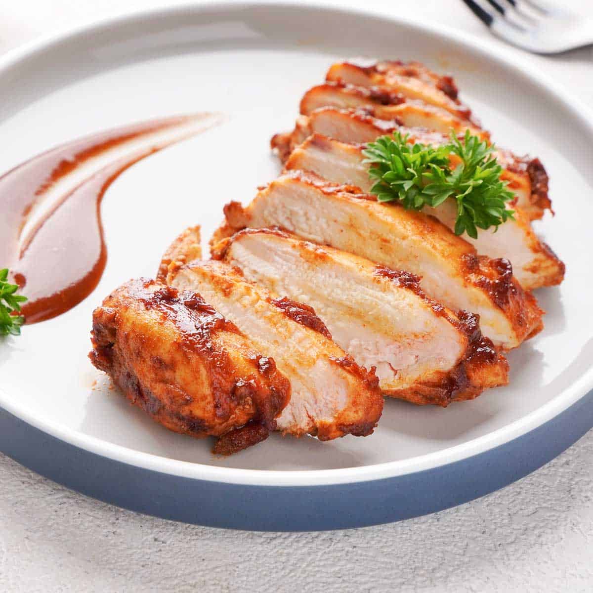 sliced barbecue chicken breast on white plate with extra sauce garnish