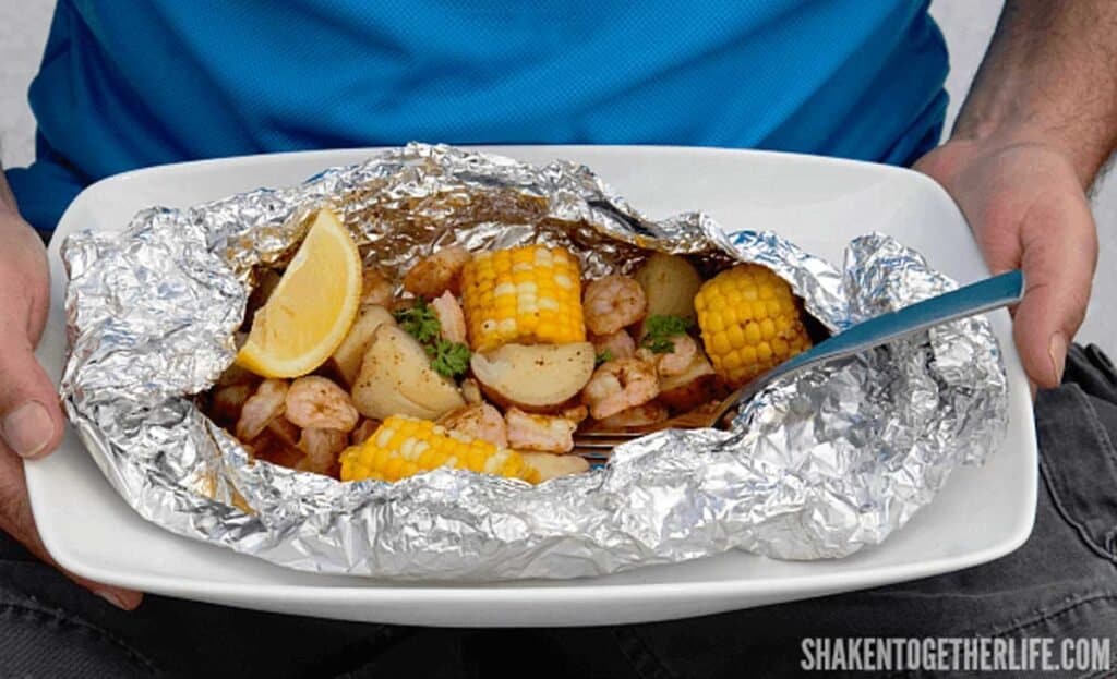 hands holding platter of shrimp boil in foil packet