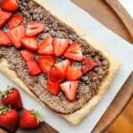 nutella tart with sliced strawberries on wood cutting board and parchment paper