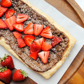 nutella tart with sliced strawberries on wood cutting board and parchment paper