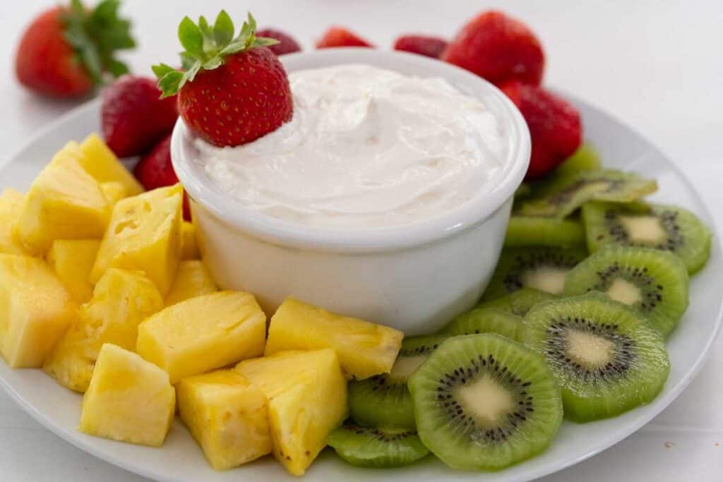 plate with cut fruit and white bowl of fruit dip