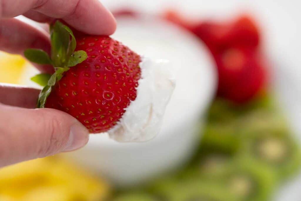 hand holding strawberry with fruit dip on it