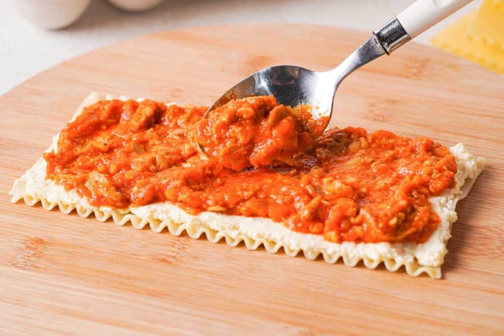 spoon adding marinara sauce to lasagna roll up