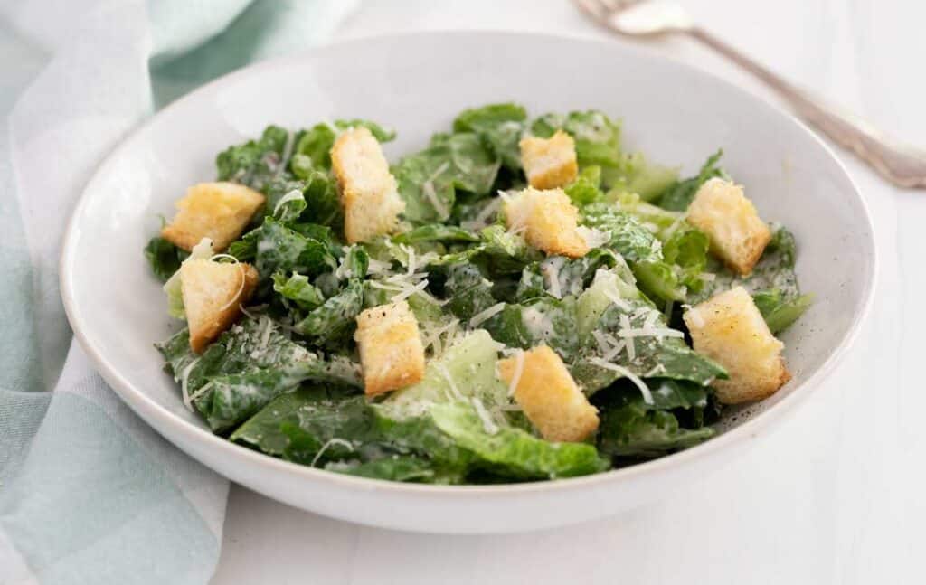 white bowl with caesar salad and fork in background