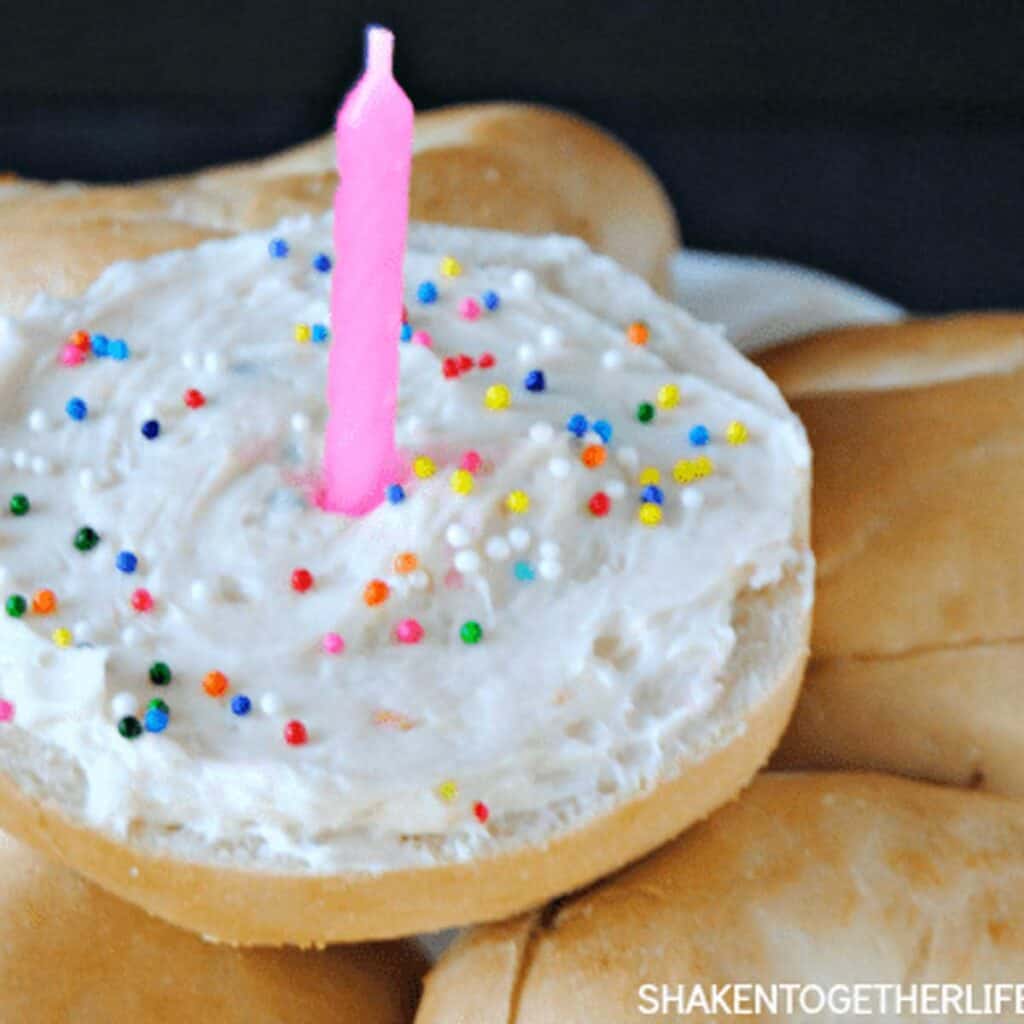 mini bagel with birthday cake cream cheese, sprinkles, and a candle