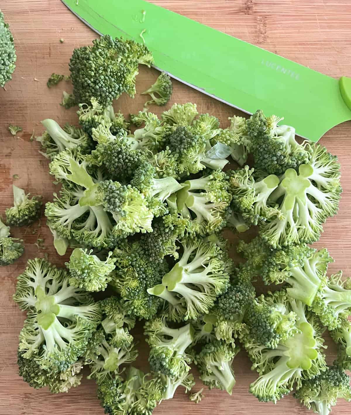 cutting board with chopped broccoli and green butchers knife