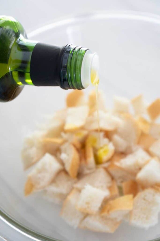 olive oil pouring over chunks of bread for croutons