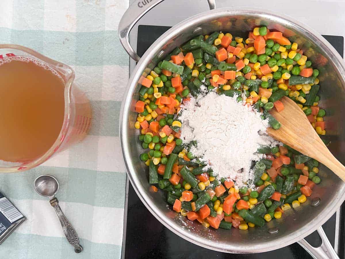 adding flour to mixed vegetables in skillet