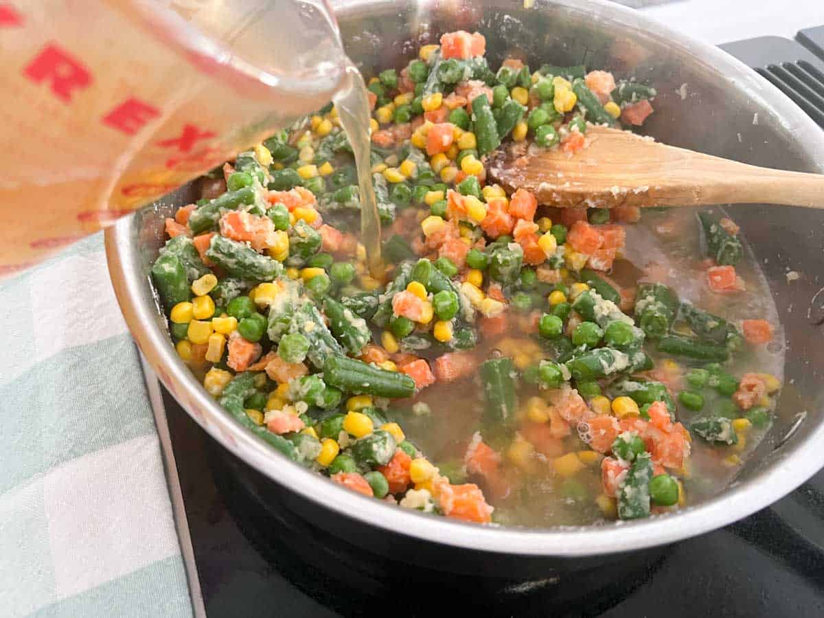 pouring broth into skillet with mixed vegetables