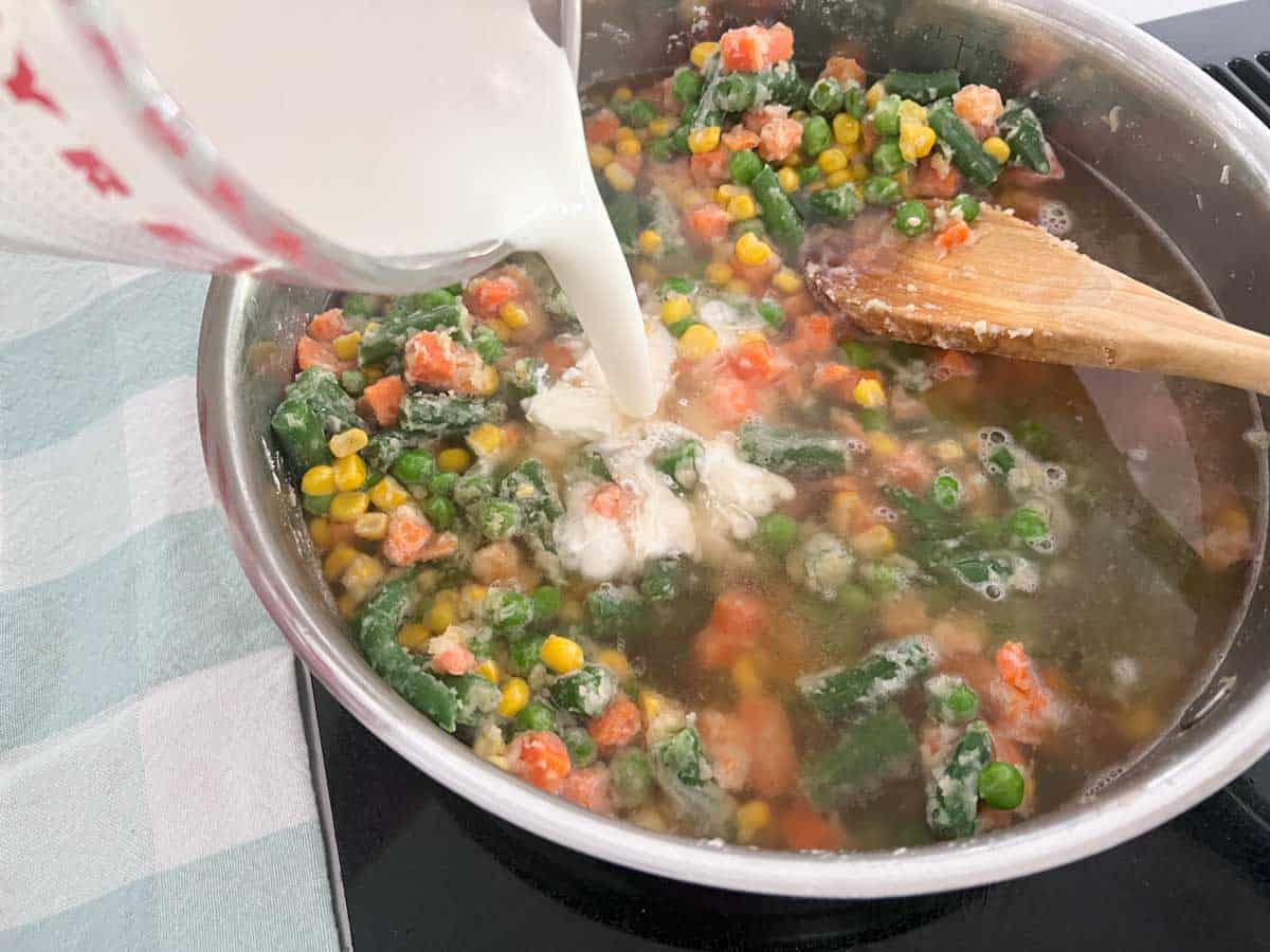 pouring cream into skillet with mixed vegetables