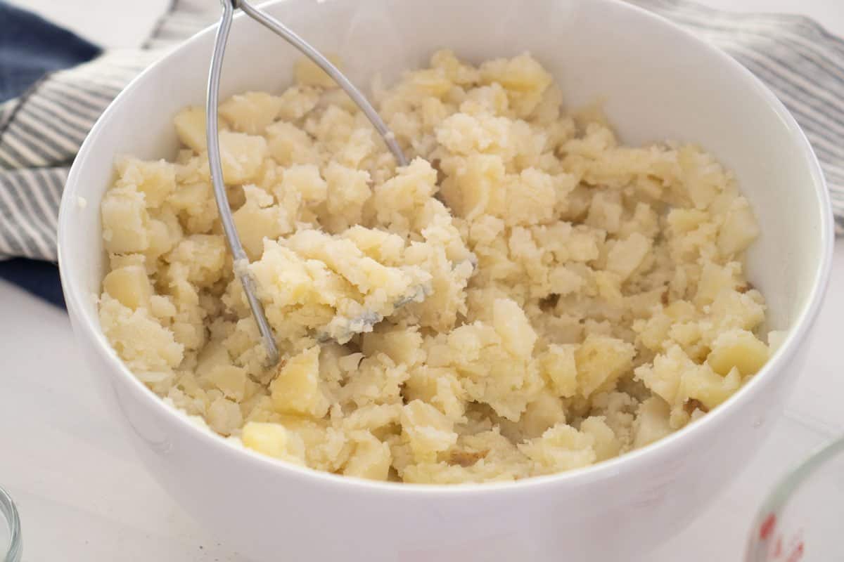 mashing potatoes with potato masher in white bowl