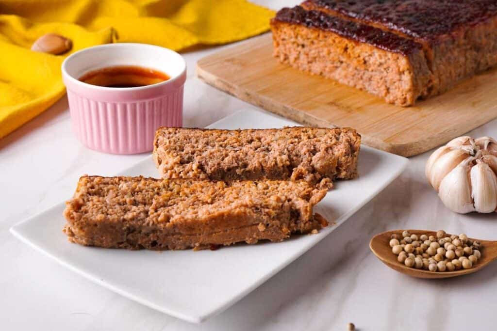 two slices of meatloaf on white plate with full meatloaf in background