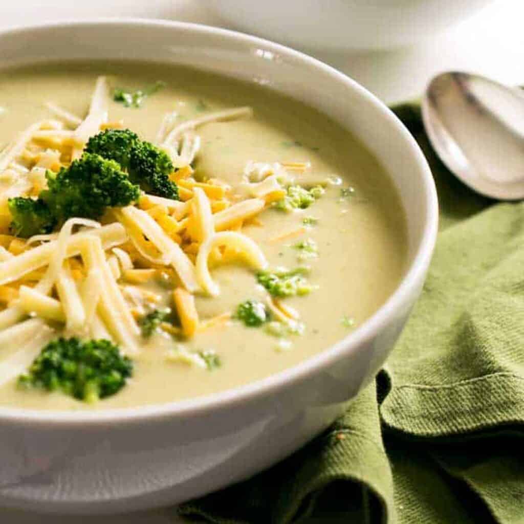 broccoli cheese soup in a white bowl topped with shredded cheese