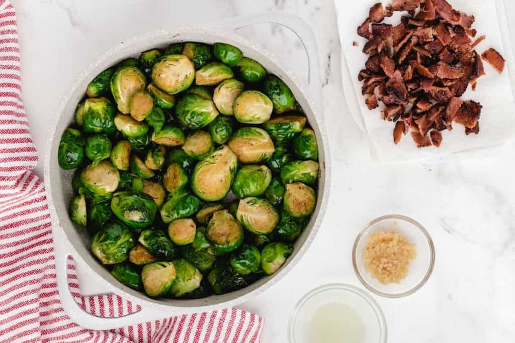 cooked brussel sprouts in dutch oven with crumbled bacon to the side