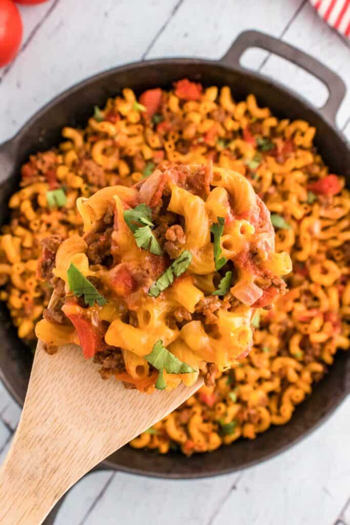 wooden spoon holding ground beef taco mac and cheese over skillet