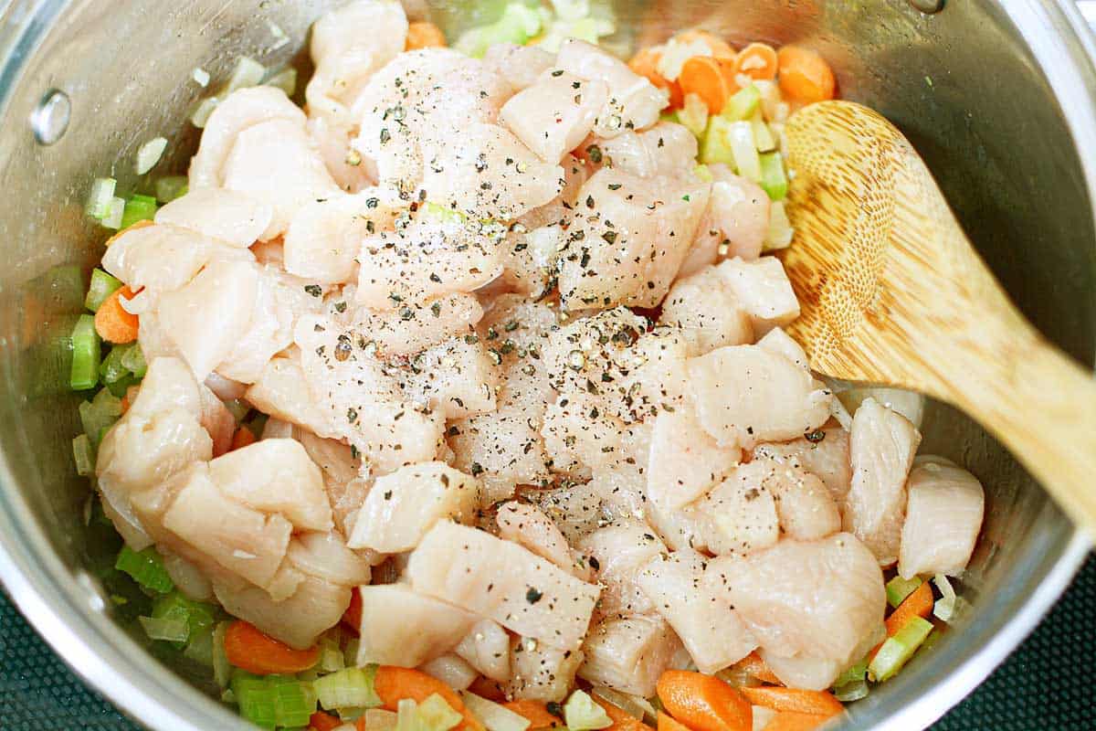 raw cubed chicken and vegetables in pot with wooden spoon