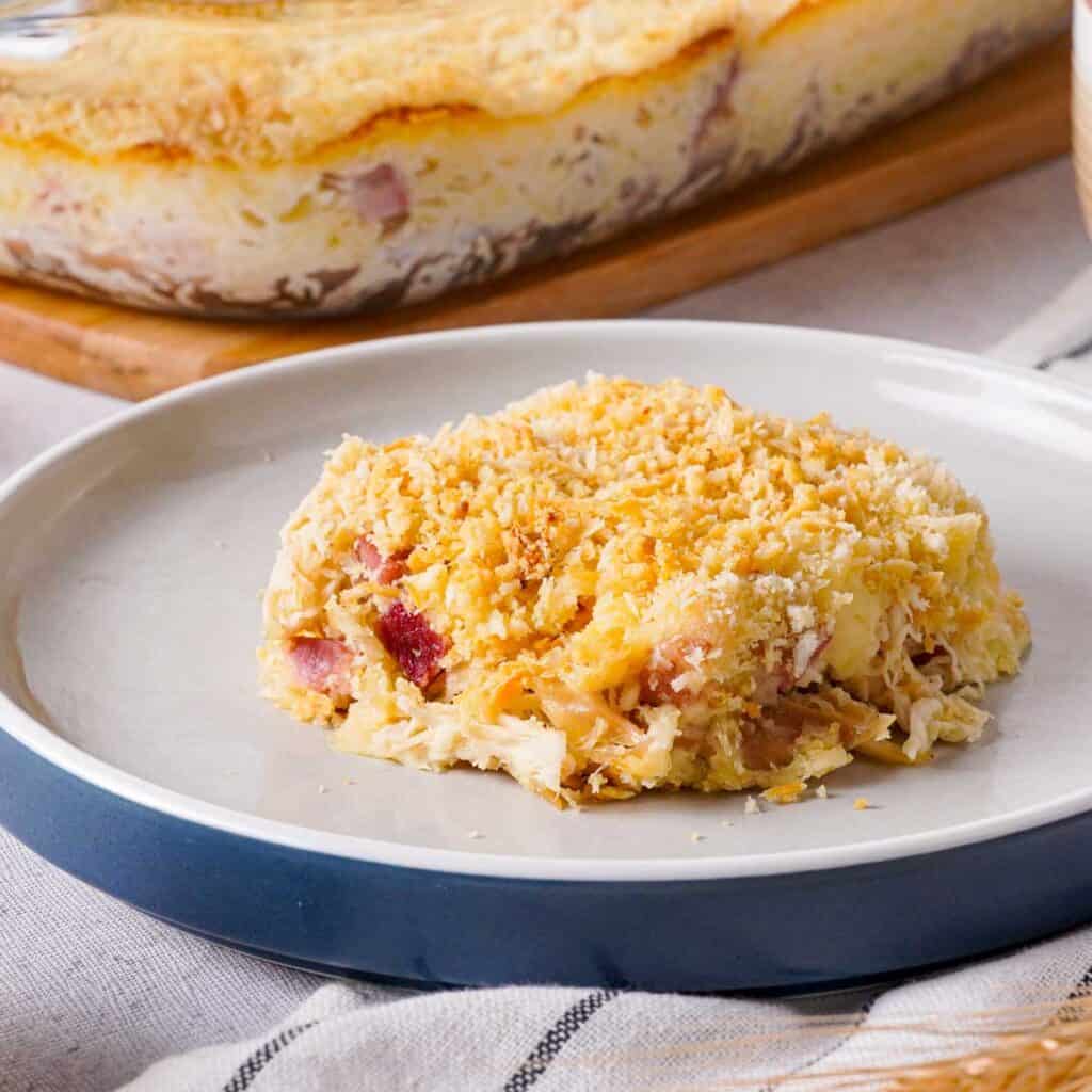 piece of chicken cordon bleu casserole on white plate with casserole dish in background