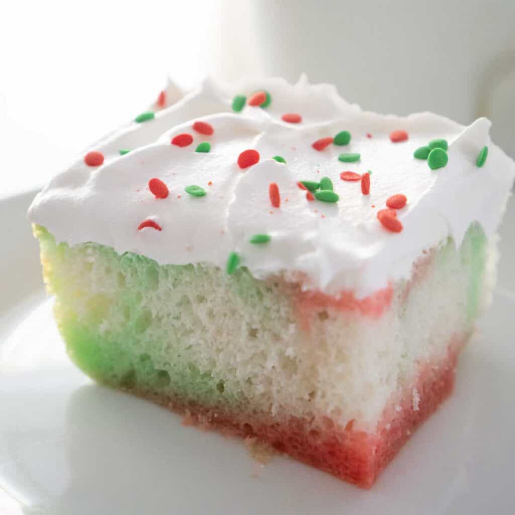 close up of a piece of Christmas poke cake topped with whipped cream and red and green sprinkles