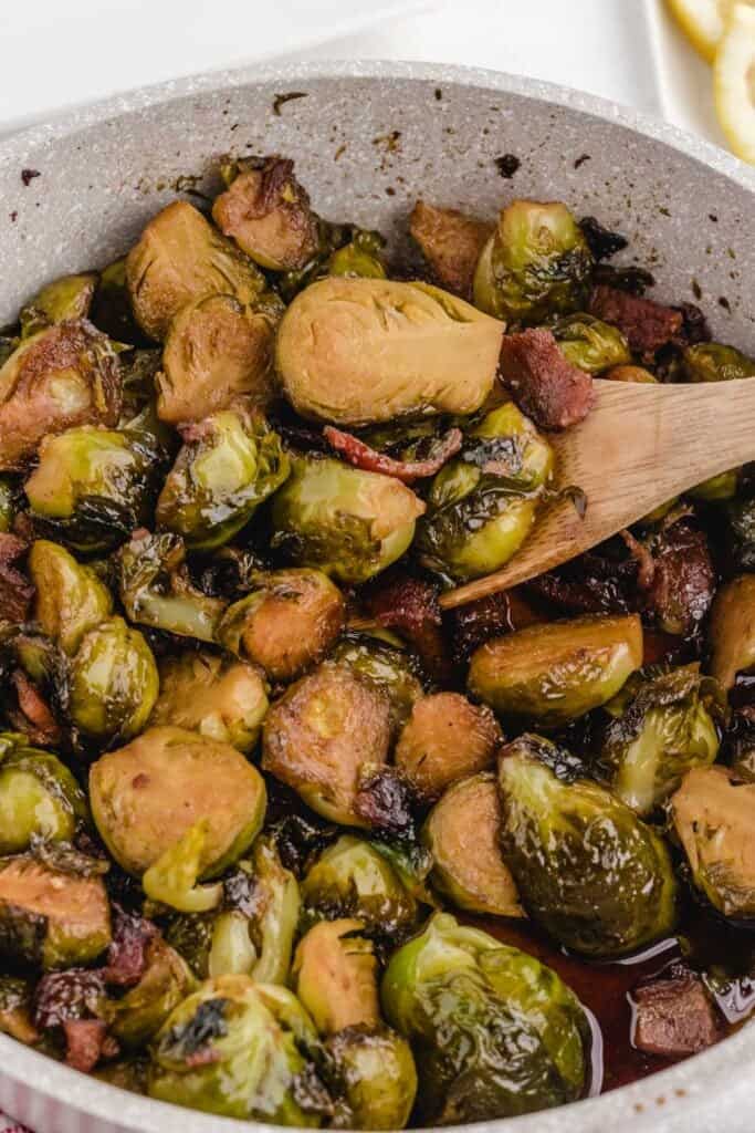 close up of brown sugar brussels sprouts with wooden spoon in pan
