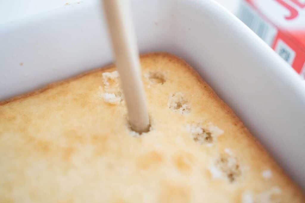 handle of wooden spoon poking holes in a cake