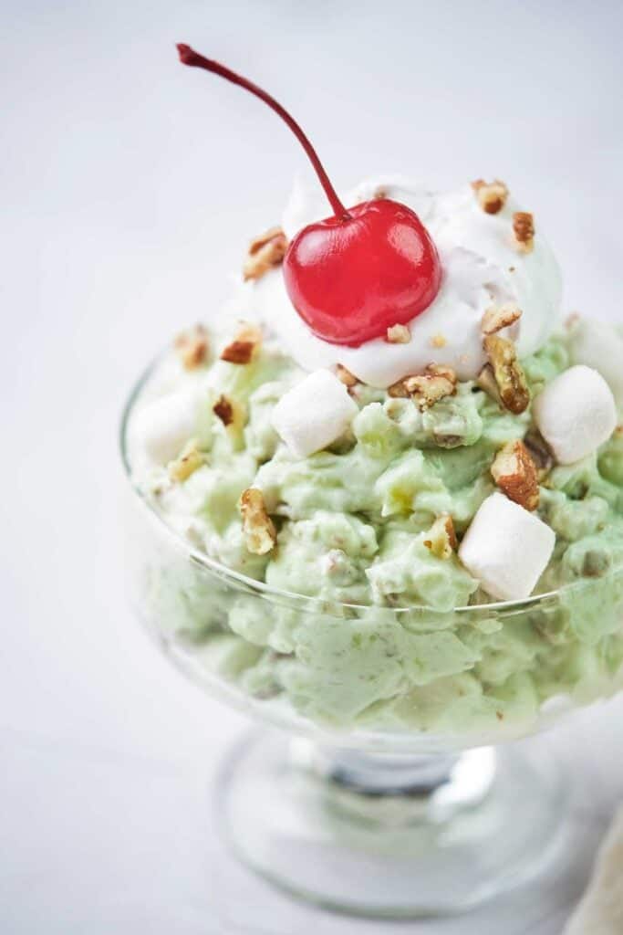 pistachio fluff salad in a glass dish topped with a maraschino cherry