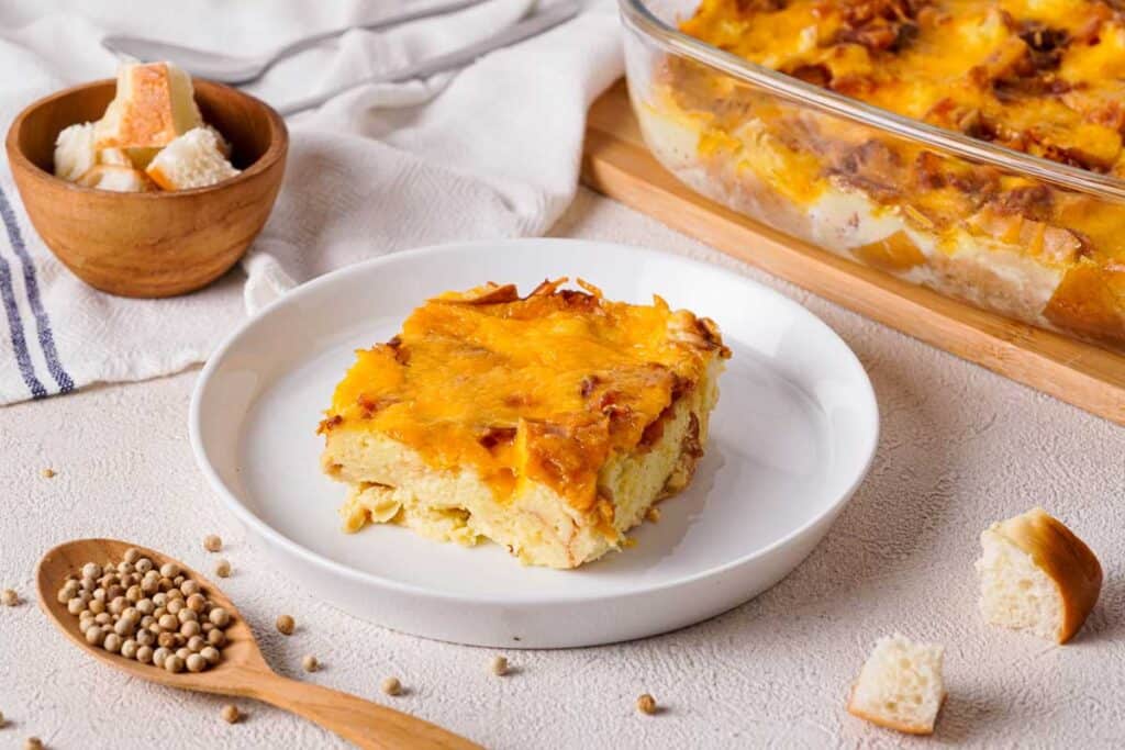 piece of bagel breakfast casserole on white plate with remaining casserole in background