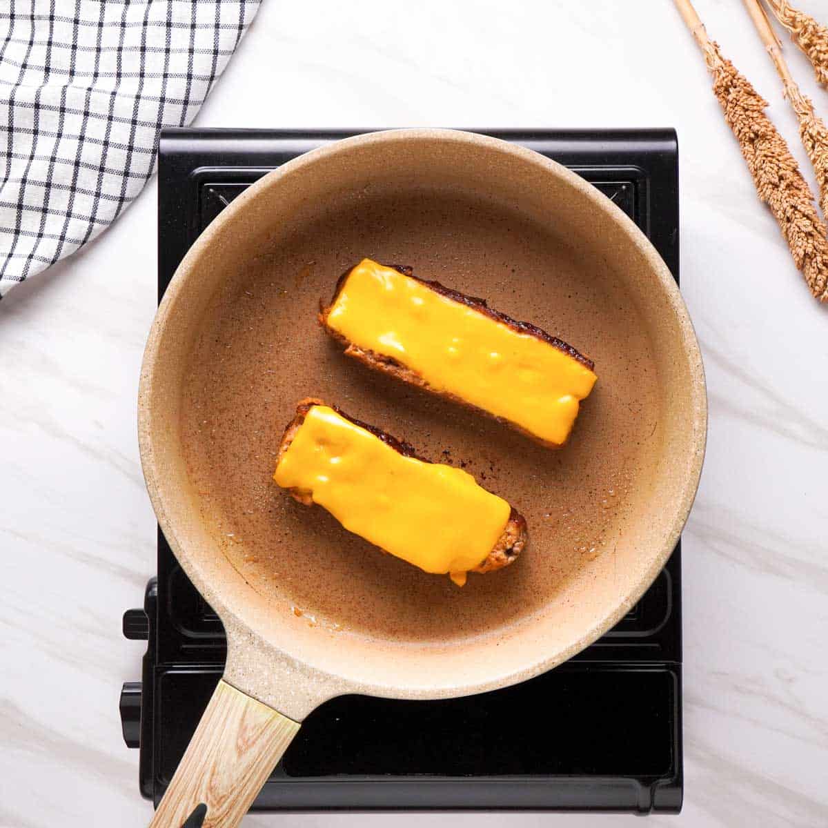 two meatloaf slices topped with cheese in small skillet