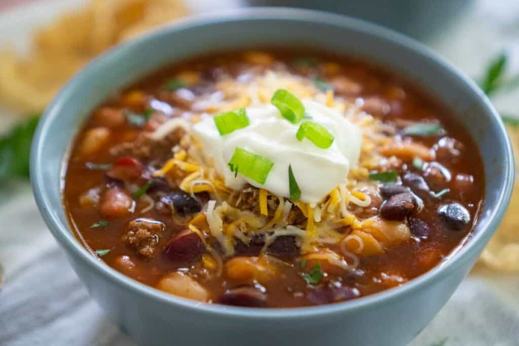 taco soup in blue bowl with sour cream and green onion