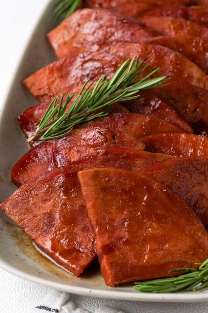 sliced bourbon glazed ham with rosemary sprig