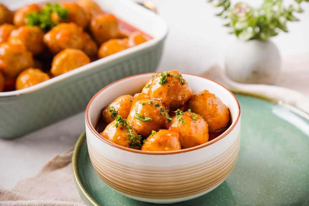 apple jelly meatballs in bowl on table with more in the background