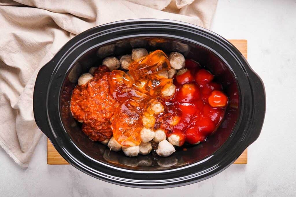 meatballs in a slow cooker topped with apple jelly, pizza sauce, and ketchup