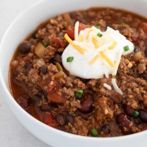 white bowl with stovetop chili topped with sour cream, cheese, and green onion