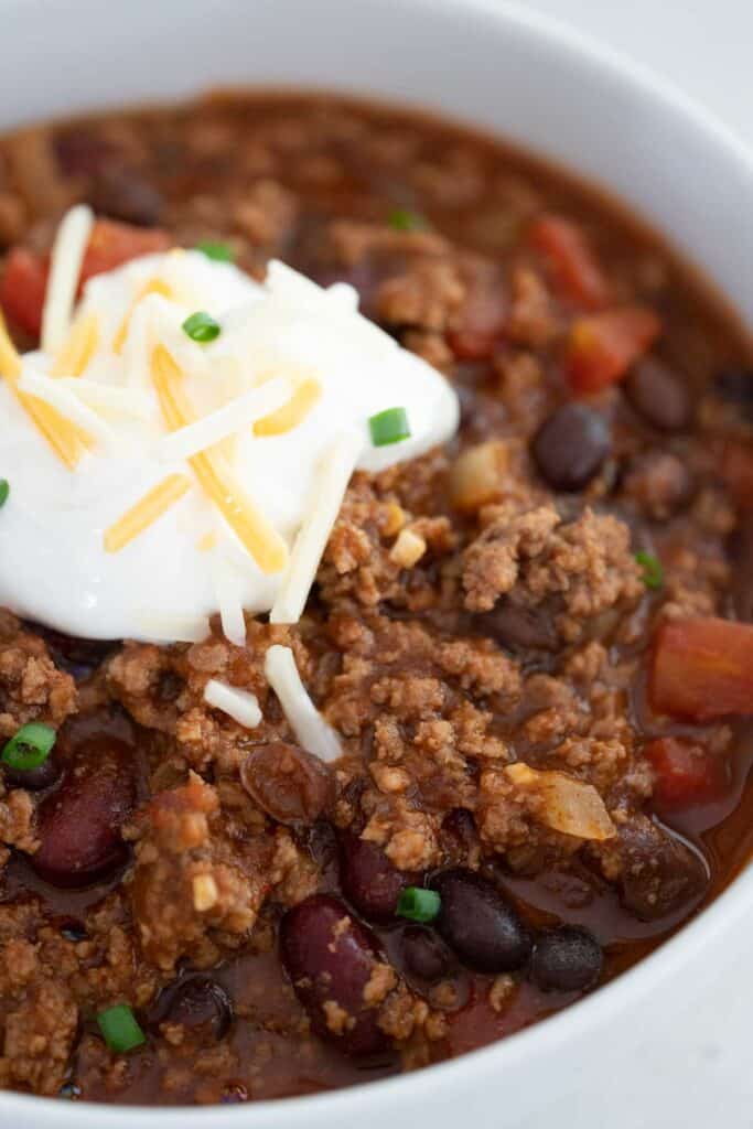 close up of white bowl with stovetop chili topped with sour cream