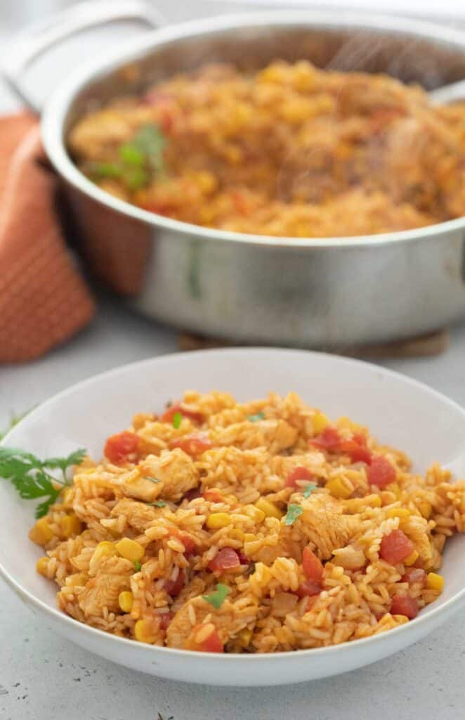 white bowl with Mexican chicken and rice with skillet in background