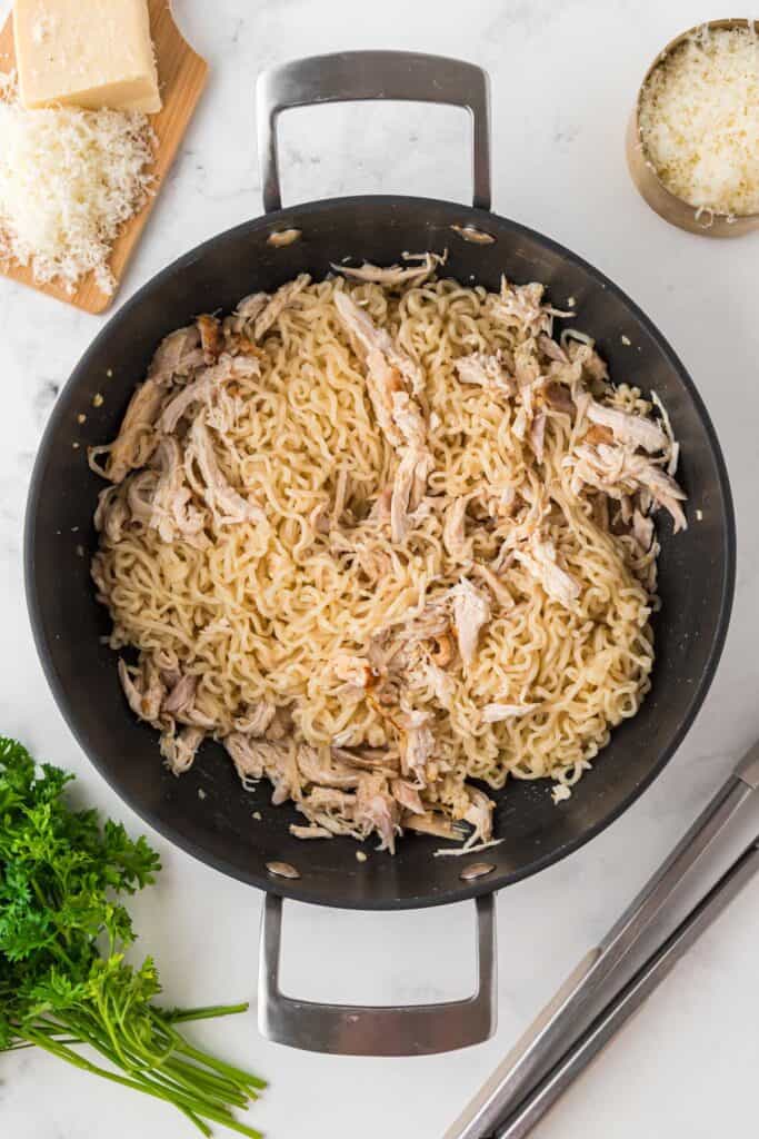 adding ramen noodles to skillet of chicken