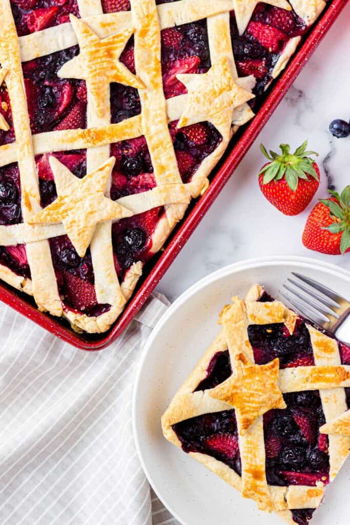 piece of berry slab pie on white plate with remaining slab pie next to it