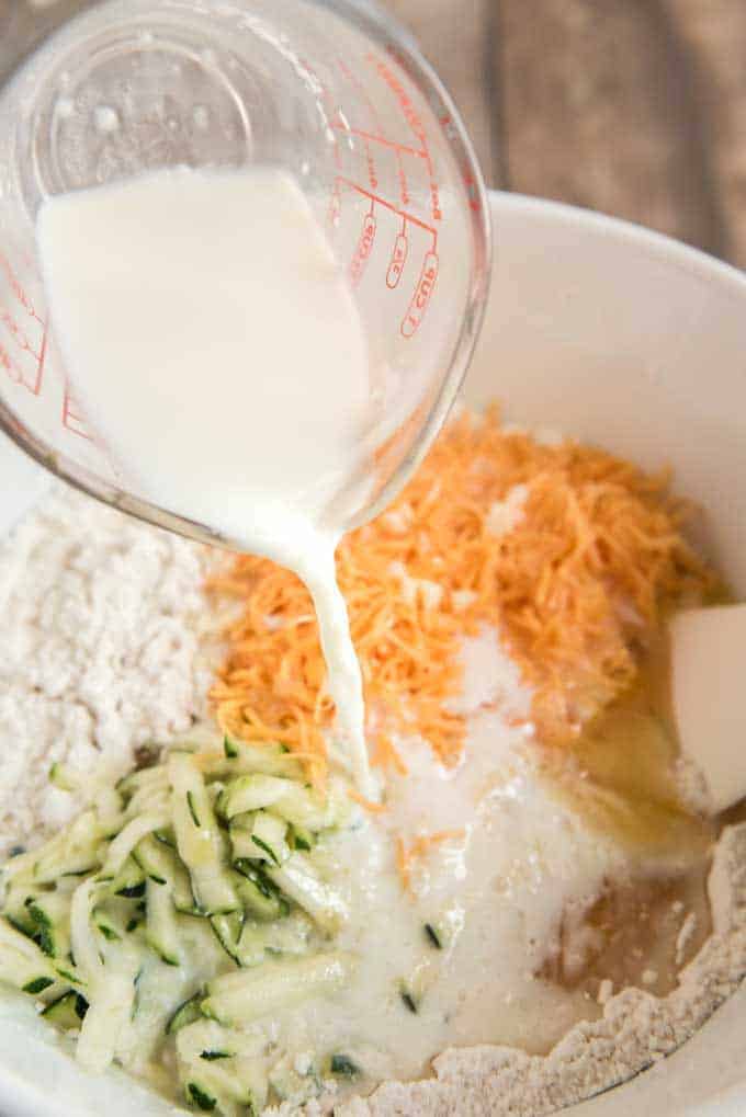 pouring milk into bowl with cheesy zucchini bread ingredients