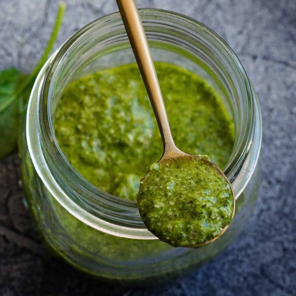 jar of pesto sauce with spoonful balancing on top