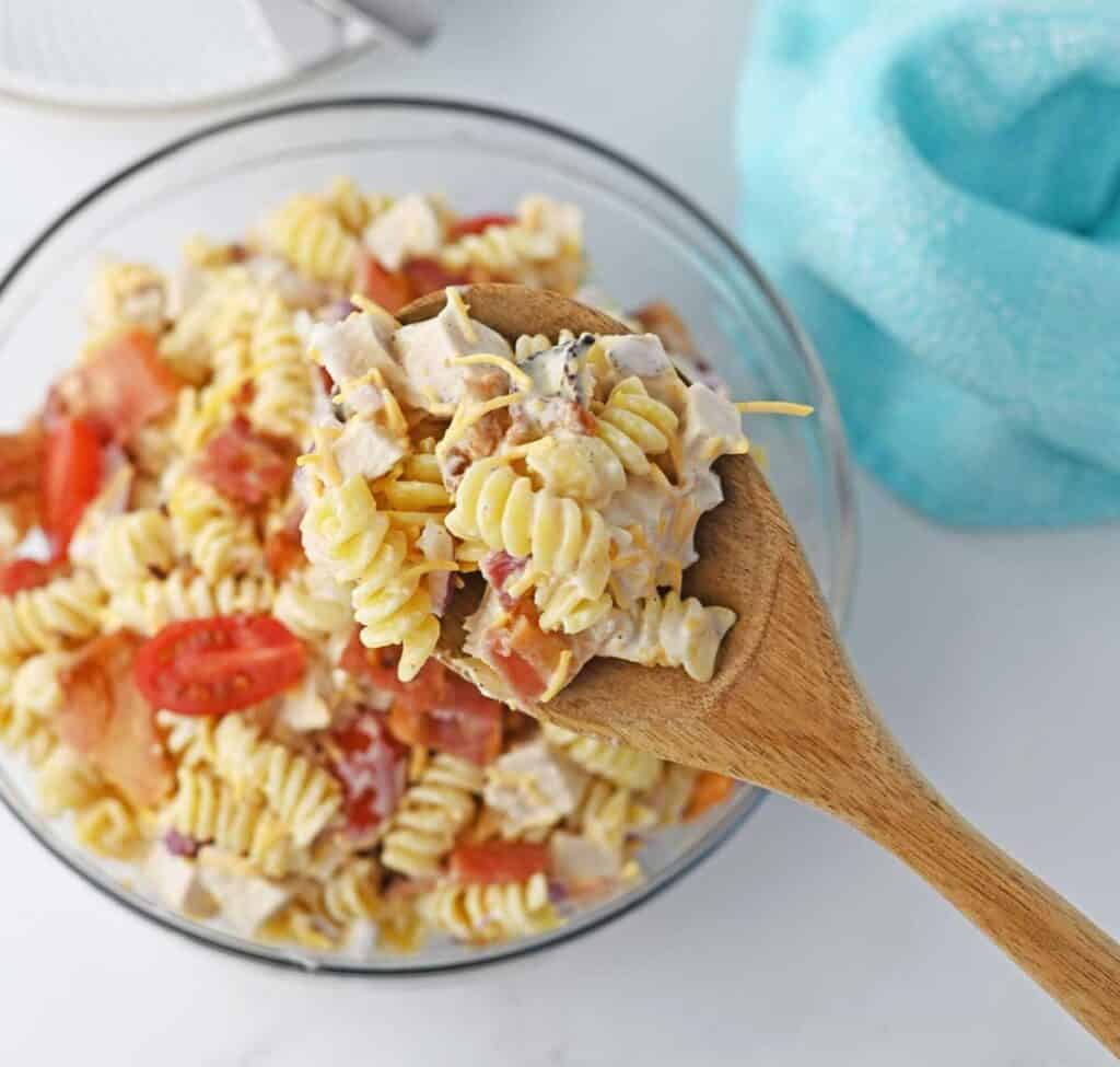 wooden spoon with chicken bacon ranch pasta salad held over bowl