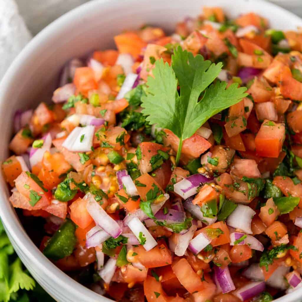 close up of pico de gallo in white bowl topped with cilantro leaf