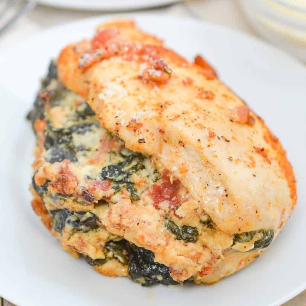 cheese, bacon, and spinach stuffed chicken breast on white plate