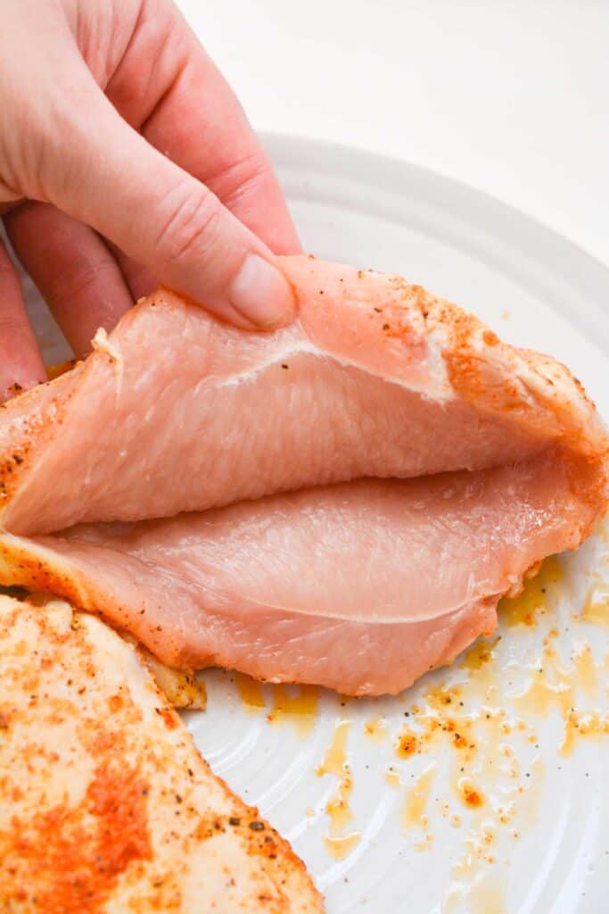 hand holding pocket of raw chicken breast open for stuffing