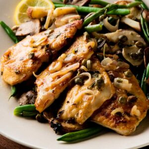 chicken piccata on white plate with green beans