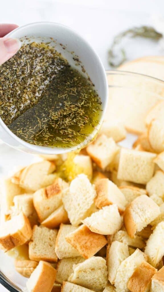 pouring herb butter over bread cubes